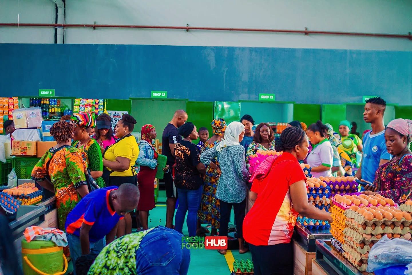 A busy market hall with shoppers around tables of egg crates.
